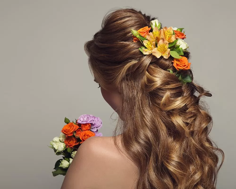 Atriz de costas segurando flor, com tranças floridas no cabelo