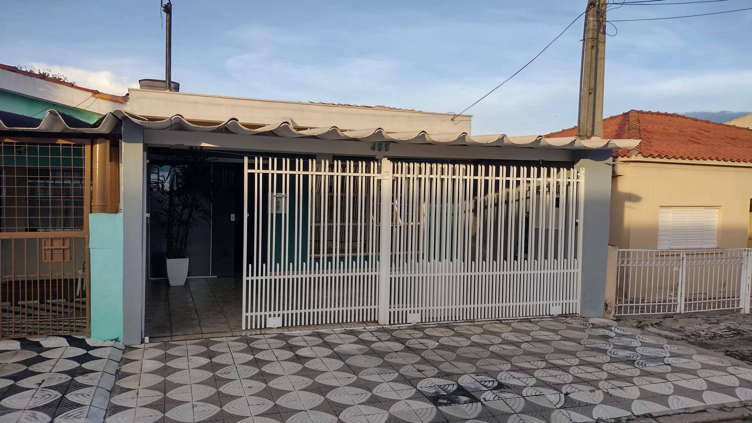Fachada de frente de casa, portão branco, calçada quadriculada