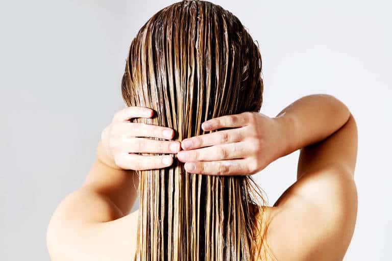 Atriz de costas tratando do cabelo umedecido e penteado