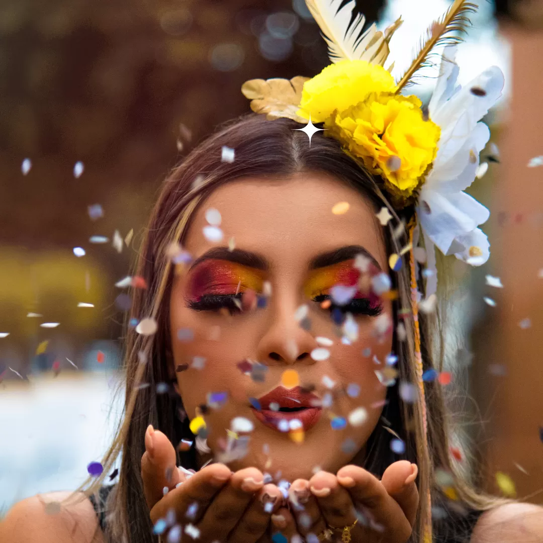 Atriz maquiada para o carnaval soprando confetes no ar